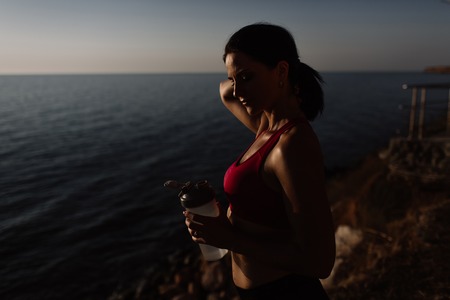 beautiful girl with sports forms sports on the beach, drinking water, jumping, running, doing different exercisesの写真素材