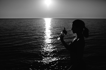 beautiful girl with sports forms sports on the beach, drinking water, jumping, running, doing different exercisesの写真素材