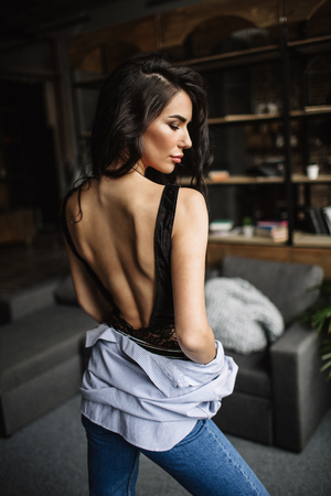 Foreground. Beautiful brunette dressed in a blue shirt and jeans in an room in the back background of a bookshelf and sofa, fashion styleの写真素材