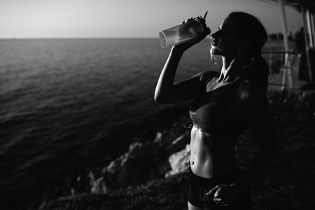 beautiful girl with sports forms sports on the beach, drinking water, jumping, running, doing different exercisesの写真素材