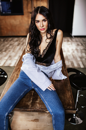 Beautiful brunette in the kitchen, modern housewife, fashion, wooden brown furniture, dressed in blue jeans and a blue shirtの写真素材