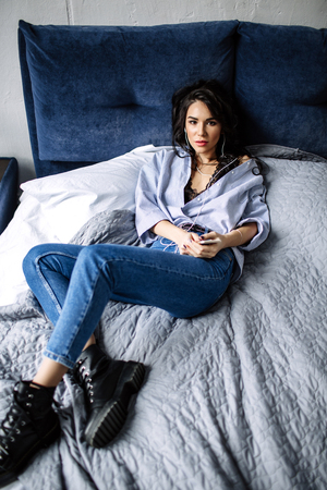 A beautiful brunette listens to music in headphones in a room near the sofa, is dressed in a shirt and blue jeans, blueの写真素材