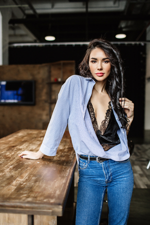 Beautiful brunette in the kitchen, modern housewife, fashion, wooden brown furniture, dressed in blue jeans and a blue shirtの写真素材