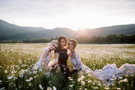 three beautiful girls brunette and blonde, brown-haired woman enjoying Daisy field, nice long dresses, pretty girl relaxing outdoor, having fun, happy young lady and Spring green nature, harmony conceptの写真素材