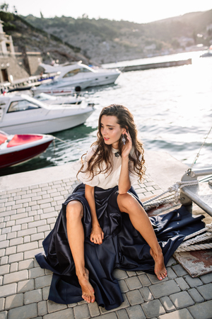 Beautiful girl walking on the pier by the sea near the yacht, boats in the blue long dressの写真素材