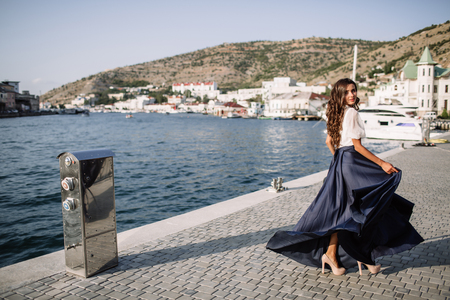 Beautiful girl walking on the pier by the sea near the yacht, boats in the blue long dressの写真素材