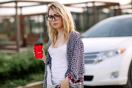 Young stylish woman in a city street near a white car.