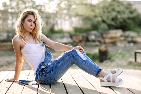 Young stylish blonde girl in denim overalls outdoors with natural daylight, a sunny day.の写真素材