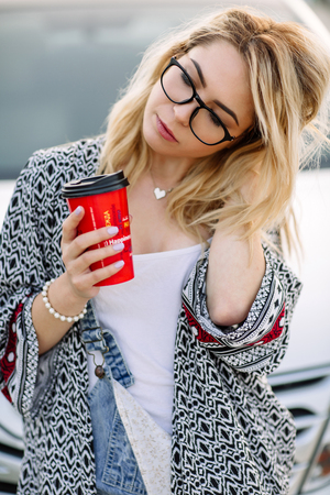 Young stylish woman in a city street near a white car.の写真素材
