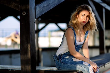 Young stylish blonde girl in denim overalls outdoors with natural daylight, a sunny day.の写真素材