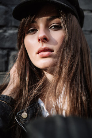 Portrait of a fashionable beautiful girl model in a cap. Men's arms embrace the faceの写真素材