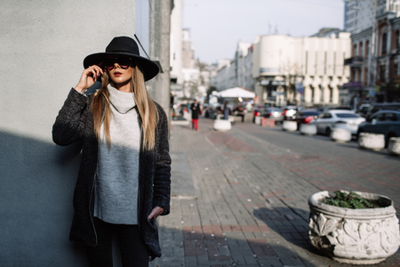 Portrait of a young beautiful fashionable girl wearing sunglasses. Model in a stylish black hat. Harmoniously similar clothes in gray tones. Street style. Women's fashion.の写真素材