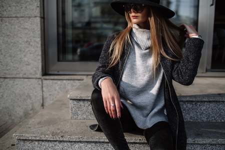 Portrait of a young beautiful fashionable girl wearing sunglasses. Model in a stylish black hat. Harmoniously similar clothes in gray tones. Street style. Women's fashion.の写真素材