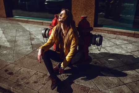 A young European woman, traveling, with long blond hair, wearing a yellow jacket, yellow sunglasses walking down the city center street, street shooting. Even light.の写真素材