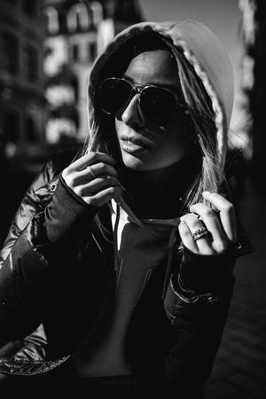 Street fashion concept - portrait of a beautiful girl sitting outside, blue jeans, sunglasses, hard lights, red jacket, autumn weatherの写真素材