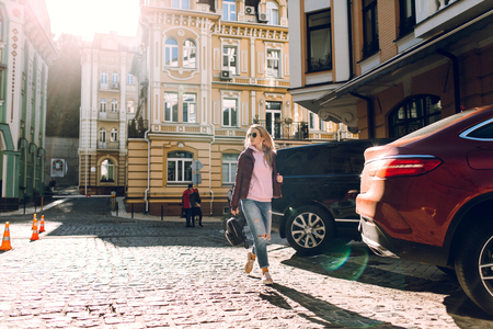 Street fashion concept - portrait of a beautiful girl walking outside, blue jeans, sunglasses, hard lights, red jacket, autumn weatherの写真素材