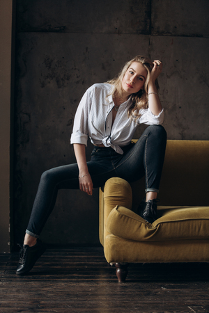 Portrait of a beautiful fashionable woman, blonde, jeans, on a yellow sofaの写真素材