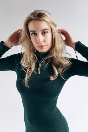 Beautiful fashionable sexy blonde model with flying long hair in a green dress on a gray backgroundの写真素材