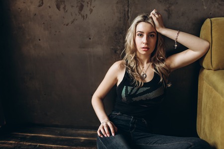 Portrait of a beautiful fashionable woman, blonde, jeans, brown backgroundの写真素材