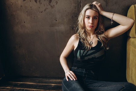 Portrait of a beautiful fashionable woman, blonde, jeans, brown backgroundの写真素材