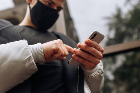 Brunette in a black T-shirt and jacket in a black face mask. Talking on the phone. Black stylish face mask during the pandemic corona virus. Handmade cotton face mask to protect against viruses and bacteria.の写真素材