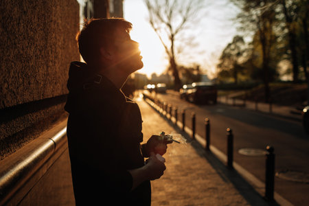 Young man smokes at sunset in the middle of the city