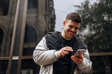 Portrait of happy young man walking on the street and looking aside while talking by his phone.