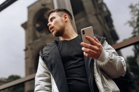 Portrait of happy young man walking on the street and looking aside while talking by his phone.の写真素材
