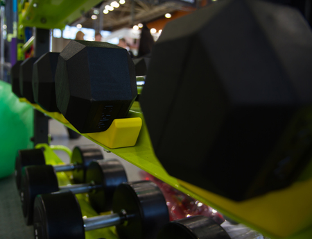 Dumbbells in gym, close up many on the rack in sport fitness centre. Black rubber hexagonal dumbbells on the shelf in the storeの写真素材
