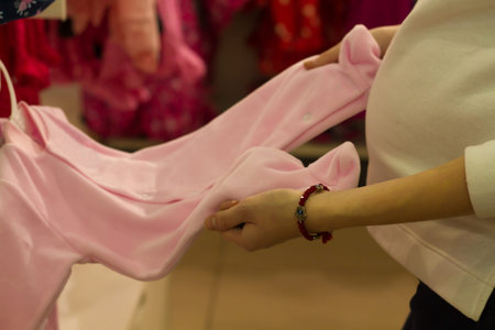 Shopping young woman, manual viewing stand pink suit for newborn girl in the shop. Buy in the store...