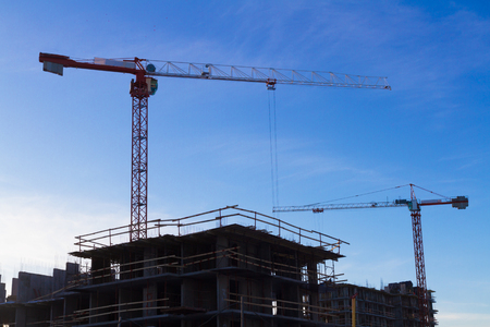 Under construction high-rise building with two cranes yellow the background of blue skyの写真素材