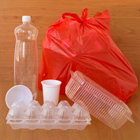 Plastic household products and a red bag with garbage on a brown background. The concept of separate...