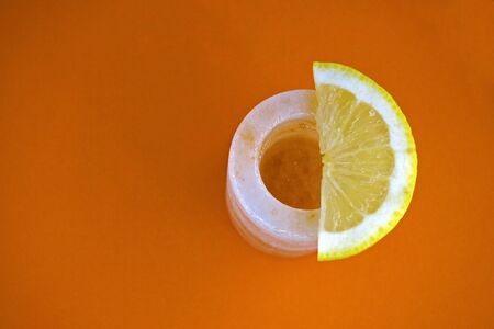 A glass of tequila with a slice of lemon is on an orange background. View from above. Close-up. Unusual tableware made from pressed Himalayan salt for an alcoholic strong drink. Copy space.の写真素材