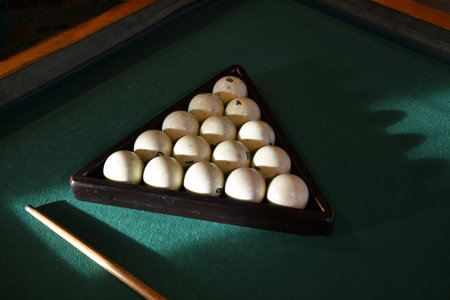 Old white billiard balls folded in a wooden triangle on a table with green cloth. Accessories for...