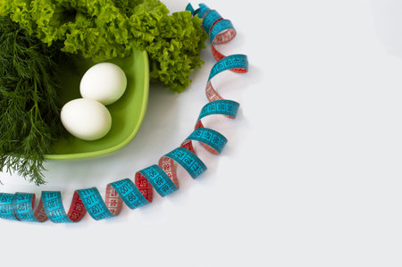 A blue meter tape rolled out in a serpentine next to a plate of herbs and chicken eggs. Proper...