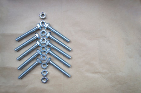 New metal bolts and nuts are stacked on crumpled brown packing paper in the shape of a Christmas tree. Household goods for home and renovation. View from above. Copy space for text. Flat lay.の写真素材