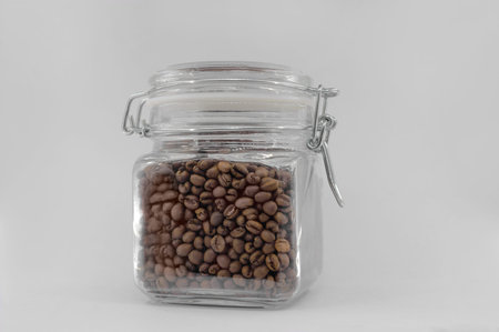 A glass jar filled with coffee beans and closed with a clip-on lid. Isolated on light gray...