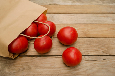 Fresh tomatoes rolled out of an eco-friendly paper bag onto a wooden deck.の写真素材