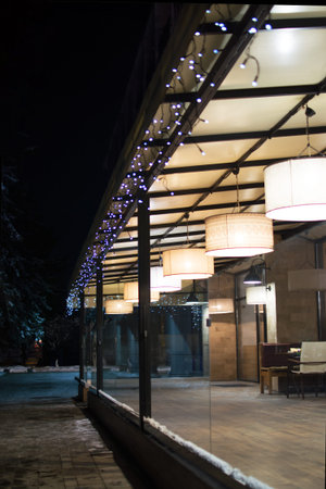Outdoor cafe terrace on a winter evening. Soft, warm light from lamps with large round lampshade.の写真素材