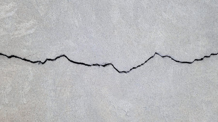 Cracked concrete surface covered with gray cement mortar. One long, winding crack in the wall....