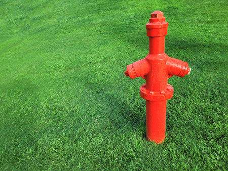 Bright red fire hydrant stands on a freshly mown lawn. Old fire pipe of the city fire extinguishing system against the background of green grass of the lawn. Selective focus, front view. Copy spaceの写真素材