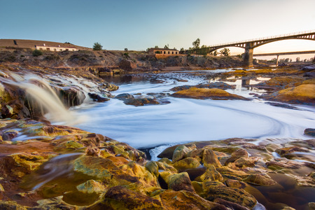 Red river with small waterfall under the bridge. Silk effect with long exposureの写真素材