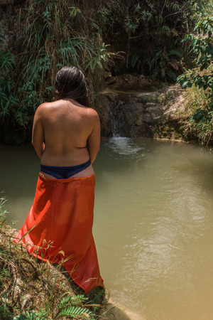 young woman in underwear without brassier standing on the edge of a natural lake covering her legs with an orange blanketの写真素材