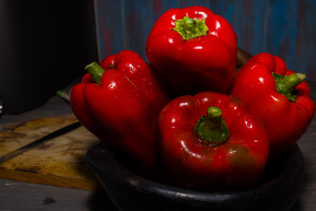 FRESH RED PEPPERS IN THE FOREGROUND IN BLACK CLAY BOWL ON RUSTIC WOOD TABLEの写真素材