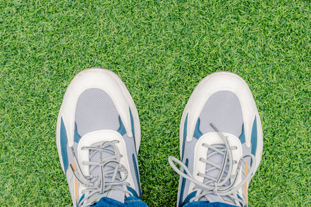 overhead view of feet with sports sneakers on green artificial grass and space for text
