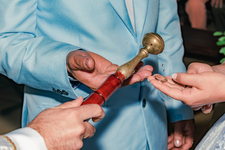 detail of the hand of a priest blessing the rings of a couple with holy water at a weddingの写真素材
