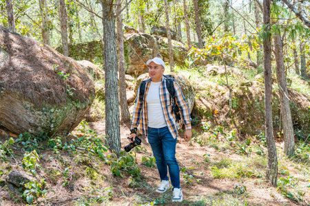 Latin American male photographer stands in the forest, carefully observing the landscape in search...