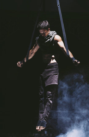 Acrobat shows his strength by spreading hands in difficult pul-up on the slings