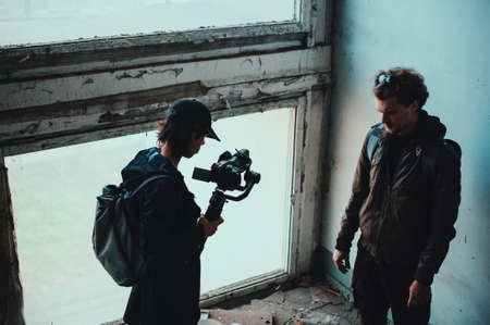 Long haired operator filming curly guy in destroyed building at windowの写真素材