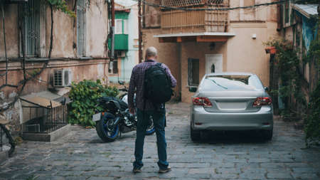 Back of bald man in narrow lane near car and motoの写真素材